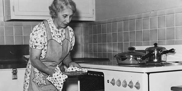 elderly woman removes pie from oven